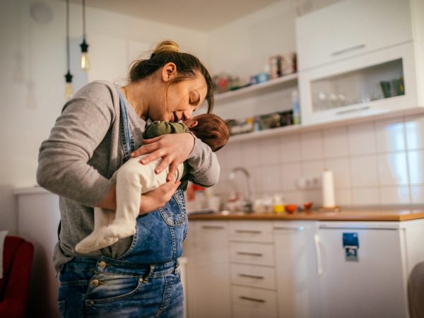 FAMILY COMMUNITY Young mum with newborn on kitchen cuddling and kissing