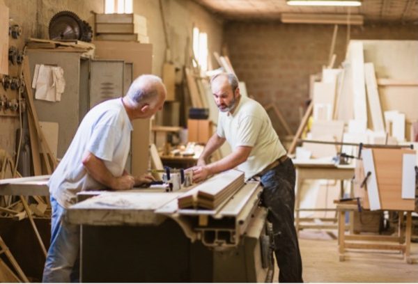 Two men measuring wood and chatting in a woodworking shed